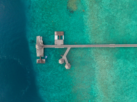 Aerial view of a wooden pier and overwater bungalows stretching over deep blue and turquoise waters Hoarafushi Thiladhunmathee Uthuruburi Maldives. Aerial view of a wooden pier and overwater bungalows stretching over deep blue and turquoise waters Hoarafushi Thiladhunmathee Uthuruburi Maldives.