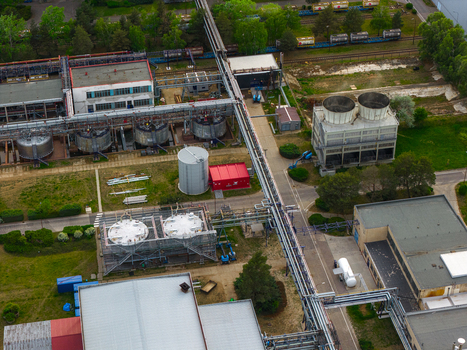 Aerial view of an industrial facility featuring large storage tanks cooling towers and complex pipeline networks surrounded by green trees in Breclav South Moravian Region Czechia.