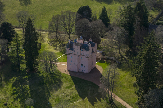 Aerial view of Craigievar Castle with its iconic pink walls surrounded by lush green lawns and tall trees Craigievar Scotland United Kingdom.