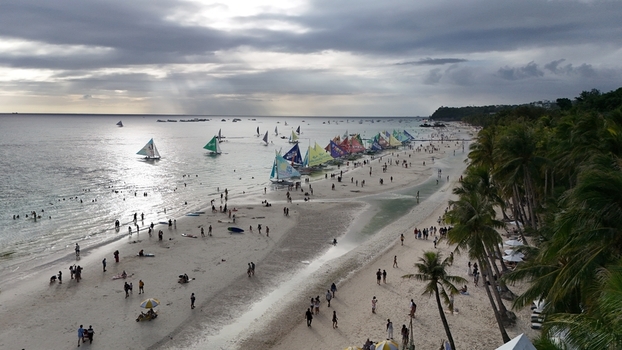 Malay Philippines 02 May 2026 Aerial view of Boracay Island featuring the white sand beach palm trees and colorful sailboats on the water under a cloudy sky.