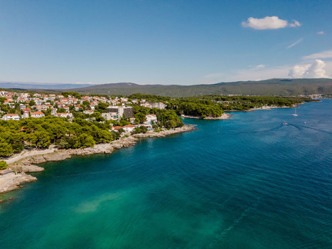 Aerial view of the coastal town of Krk featuring red roofed houses nestled among lush pine forests along the turquoise Adriatic Sea Krk Primorje Gorski Kotar Croatia.