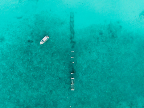 Aerial view of a solitary white boat gracefully drifting over crystal clear turquoise waters revealing a haunting submerged structure below Hoarafushi Thiladhunmathee Uthuruburi Maldives. Aerial view of a solitary white boat gracefully drifting over crystal clear turquoise waters revealing a haunting submerged structure below Hoarafushi Thiladhunmathee Uthuruburi Maldives.