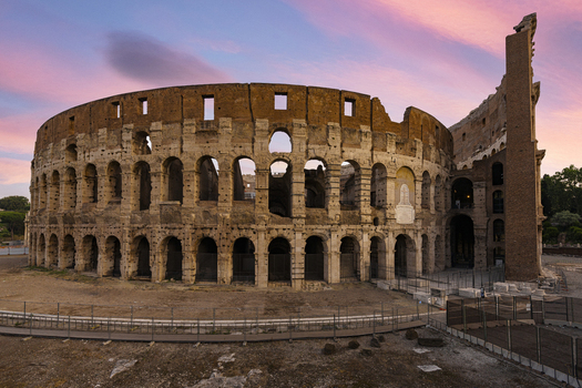 View of the Colosseum with its iconic stone arches under a vibrant pink and purple sunset sky Rome Lazio Italy. View of the Colosseum with its iconic stone arches under a vibrant pink and purple sunset sky Rome Lazio Italy.