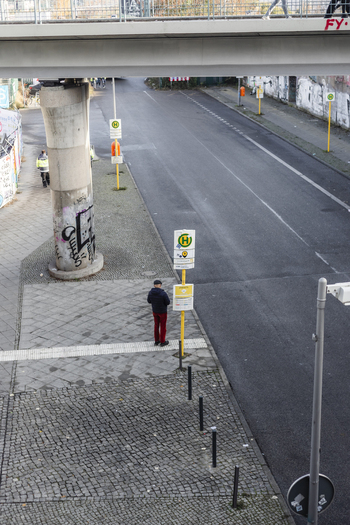 Berlin Germany 23 November 2022 View of a man standing at a bus stop under a concrete bridge overpass with an empty asphalt road and graffiti on a pillar. Berlin Germany 23 November 2022 View of a man standing at a bus stop under a concrete bridge overpass with an empty asphalt road and graffiti on a pillar.