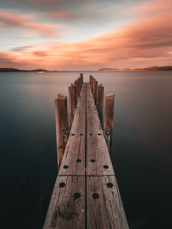 View of a wooden jetty extending into the calm water of the bay at sunset with soft pink clouds in the sky in Little Grove Western Australia Australia. View of a wooden jetty extending into the calm water of the bay at sunset with soft pink clouds in the sky in Little Grove Western Australia Australia.