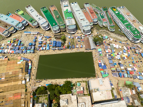Aerial view of a multitude of colorful boats docked next to a vibrant green field surrounded by tents and structures Charmonai Barisal Division Bangladesh. Aerial view of a multitude of colorful boats docked next to a vibrant green field surrounded by tents and structures Charmonai Barisal Division Bangladesh.