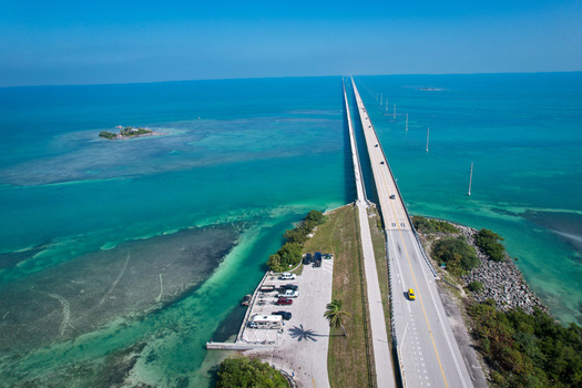 Aerial view of The Overseas Highway stretching across turquoise waters and coral reefs under a clear blue sky in Key Largo Florida United States. Aerial view of The Overseas Highway stretching across turquoise waters and coral reefs under a clear blue sky in Key Largo Florida United States.