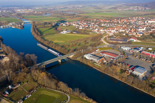 Aerial view of a cargo barge navigating a river under a bridge near the Liapor GmbH Co. KG facility and the village of Hallerndorf Bayern Germany. Aerial view of a cargo barge navigating a river under a bridge near the Liapor GmbH Co. KG facility and the village of Hallerndorf Bayern Germany.