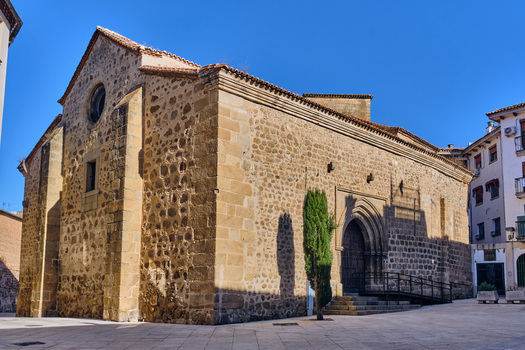 Plasencia Spain 03 December 2025 View of Iglesia del Salvador with its stone facade arched entrance and a single cypress tree in a paved plaza under a clear blue sky. Plasencia Spain 03 December 2025 View of Iglesia del Salvador with its stone facade arched entrance and a single cypress tree in a paved plaza under a clear blue sky.