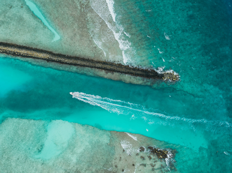 Aerial view of a boat slicing through the turquoise channel guarded by a dark stone barrier creating a striking contrast of colors Vashafaru Island Thiladhummathi Atoll Maldives. Aerial view of a boat slicing through the turquoise channel guarded by a dark stone barrier creating a striking contrast of colors Vashafaru Island Thiladhummathi Atoll Maldives.