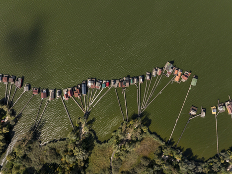 Aerial view of Bokodi Floating Village with its iconic wooden houses on stilts over the lake connected by long wooden walkways surrounded by lush green vegetation in Oroszlany Hungary. Aerial view of Bokodi Floating Village with its iconic wooden houses on stilts over the lake connected by long wooden walkways surrounded by lush green vegetation in Oroszlany Hungary.
