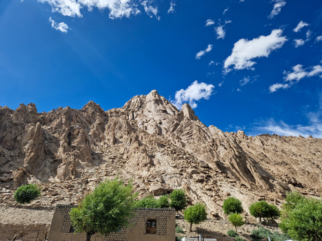 View of Shey Palace Ladakh with rugged mountain slopes green trees and a clear blue sky Shey Ladakh India.