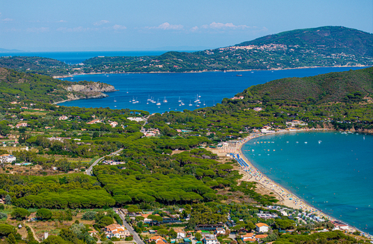 Aerial view of Lacona Beach with its turquoise water sandy shore and surrounding pine forests featuring sailboats anchored in the bay in Lacona Tuscany Italy.