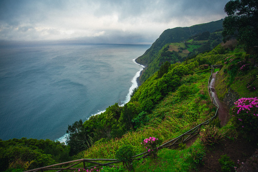 Aerial view of rugged cliffs draped in emerald vegetation meet the sapphire ocean under a moody sky Ponta Delgada Azores Portugal.