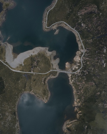 Aerial view of the mountainous landscape around Snowdon featuring dark glacial lakes and winding paths through rugged terrain in Caernarfon Wales United Kingdom.