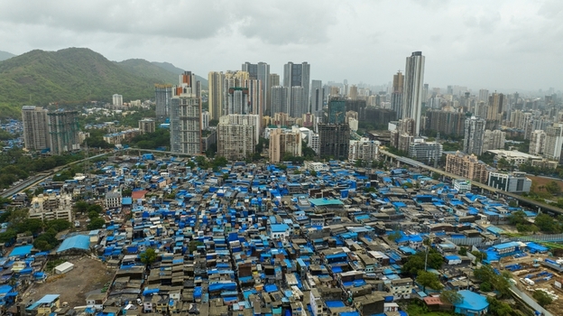 Aerial view of the dense Dharavi Slums with blue roofed structures contrasting with the modern high rise skyline of Mumbai Maharashtra India. Aerial view of the dense Dharavi Slums with blue roofed structures contrasting with the modern high rise skyline of Mumbai Maharashtra India.