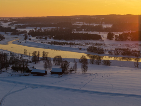 Aerial view of the winding Neris river flowing through a snow covered landscape with rural houses at sunset in Kernave Vilnius County Lithuania.