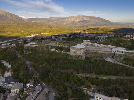 Aerial view of Gjirokaster Castle a historic fortress overlooking the stone city with distinctive rooftops surrounded by green hills and mountains in Gjirokaster Gjirokaster County Albania. Aerial view of Gjirokaster Castle a historic fortress overlooking the stone city with distinctive rooftops surrounded by green hills and mountains in Gjirokaster Gjirokaster County Albania.