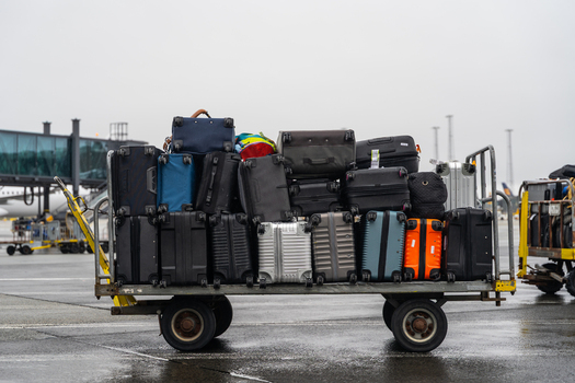 View of a baggage cart loaded with various suitcases and travel bags on an airport tarmac in Iceland. View of a baggage cart loaded with various suitcases and travel bags on an airport tarmac in Iceland.