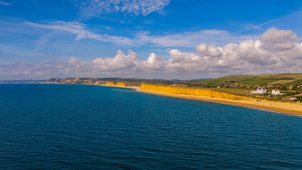 Aerial view of the iconic golden sandstone cliffs along the Jurassic Coast with the blue sea and coastal landscape in West Bay England United Kingdom. Aerial view of the iconic golden sandstone cliffs along the Jurassic Coast with the blue sea and coastal landscape in West Bay England United Kingdom.