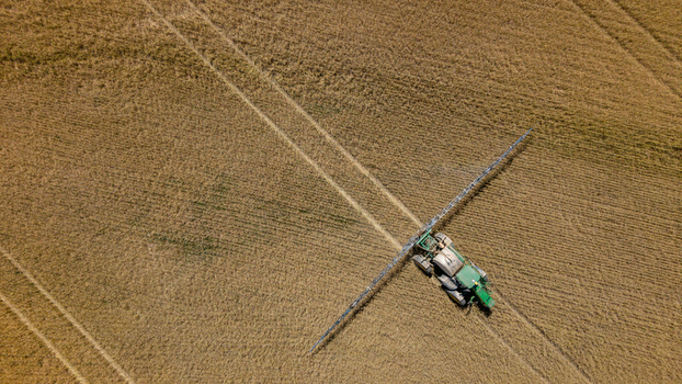 Aerial view of a tractor with long spray booms working in a golden wheat field in Philadelphia Western Cape South Africa. Aerial view of a tractor with long spray booms working in a golden wheat field in Philadelphia Western Cape South Africa.