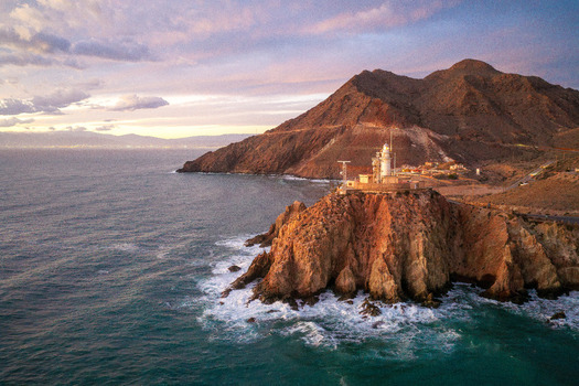 Aerial view of Lighthouse de Cabo de Gata perched on a rugged cliff overlooking the Mediterranean Sea at sunset with golden light hitting the rocky coastline San Jose Andalucia Spain. Aerial view of Lighthouse de Cabo de Gata perched on a rugged cliff overlooking the Mediterranean Sea at sunset with golden light hitting the rocky coastline San Jose Andalucia Spain.