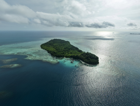 Aerial view of a verdant island embraced by turquoise shallows and deep blue waters Menjangan Kecil Island Karimunjawa Central Java Indonesia.