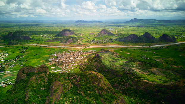 Aerial view of the rocky hills of Dass surrounded by lush green fields a winding river and rural settlements in the landscape of Bauchi Bauchi Nigeria.