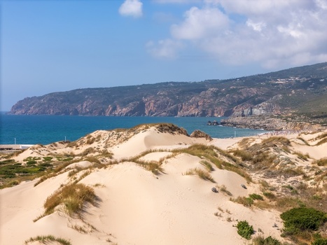 Aerial view of Praia do Guincho with its expansive sand dunes rugged cliffs and the Atlantic Ocean under a clear blue sky in Cascais Lisbon Portugal. Aerial view of Praia do Guincho with its expansive sand dunes rugged cliffs and the Atlantic Ocean under a clear blue sky in Cascais Lisbon Portugal.
