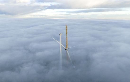Aerial view of a wind turbine and a yellow construction crane rising above a thick blanket of clouds under an overcast sky Netherlands. Aerial view of a wind turbine and a yellow construction crane rising above a thick blanket of clouds under an overcast sky Netherlands.