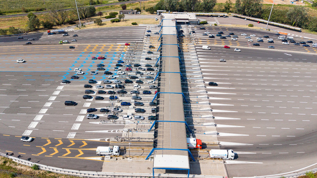 Aerial view of Milano Sud toll plaza on the A1 motorway with vehicles and trucks passing through toll gates and highway infrastructure in Melegnano Lombardy Italy.
