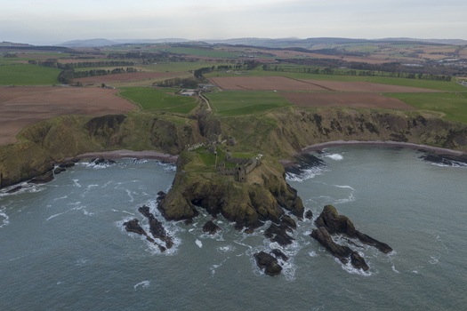 Aerial view of Dunnottar Castle ruins on a dramatic rocky cliff overlooking the sea with green fields in the background Stonehaven Scotland United Kingdom. Aerial view of Dunnottar Castle ruins on a dramatic rocky cliff overlooking the sea with green fields in the background Stonehaven Scotland United Kingdom.