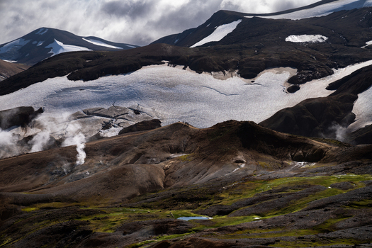 View of volcanic landscape with steaming vents and glacial ice contrasting with the green foreground creating a surreal scene Hrunamannahreppur Iceland.