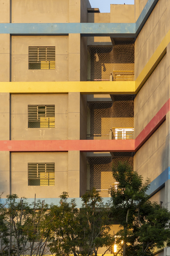 View of a modern building facade featuring colorful horizontal bands and safety netting behind green trees in Taipei City Taiwan. View of a modern building facade featuring colorful horizontal bands and safety netting behind green trees in Taipei City Taiwan.