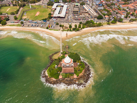 Aerial view of the Paravi Duwa Temple on a small rocky island connected by a bridge to the sandy beach and urban coastline in Matara Southern Province Sri Lanka. Aerial view of the Paravi Duwa Temple on a small rocky island connected by a bridge to the sandy beach and urban coastline in Matara Southern Province Sri Lanka.