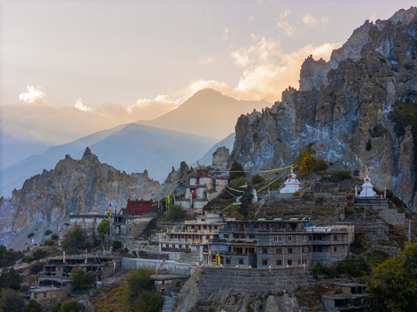 Aerial view of Braga Monastery nestled among rugged Himalayan peaks featuring traditional stone architecture white stupas and fluttering prayer flags under the golden hour light in Nepal.