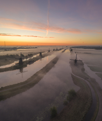 Aerial view of UNESCO World Heritage Kinderdijk windmills shrouded in morning mist along the canal under a colorful sunrise sky Kinderdijk Zuid Holland Netherlands.