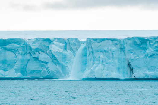 Svalbard and Jan Mayen 26 July 2025 View of a massive blue glacier wall with a waterfall of meltwater cascading into the arctic sea under an overcast sky. Svalbard and Jan Mayen 26 July 2025 View of a massive blue glacier wall with a waterfall of meltwater cascading into the arctic sea under an overcast sky.