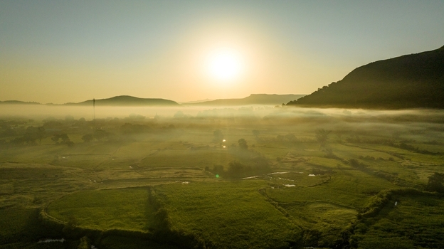 Aerial view of the misty landscape at sunrise with golden light illuminating the green fields and rolling hills in the background Igatpuri Maharashtra India.