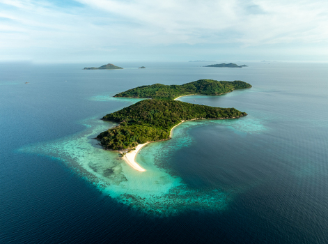 Aerial view of Malcapuya Island featuring lush green hills white sand beaches and turquoise coral reefs surrounded by deep blue ocean in Coron Mimaropa Philippines. Aerial view of Malcapuya Island featuring lush green hills white sand beaches and turquoise coral reefs surrounded by deep blue ocean in Coron Mimaropa Philippines.
