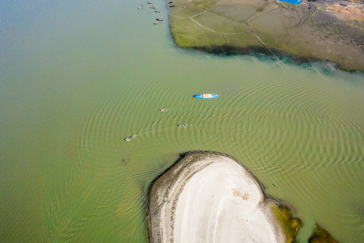 Aerial view of Kuakata beach with small fishing boats navigating the calm waters near a sandy spit and green coastline in Kuakata Barisal Division Bangladesh. Aerial view of Kuakata beach with small fishing boats navigating the calm waters near a sandy spit and green coastline in Kuakata Barisal Division Bangladesh.
