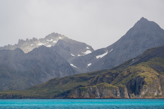 View of the rugged mountains and snow capped peaks rising above the turquoise waters of the bay near Grytviken South Georgia and the South Sandwich Islands.