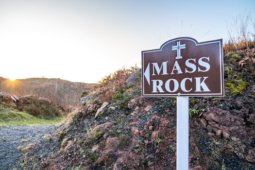 View of the Kincasslagh Mass Rock signpost set against a rocky hillside during the golden hour in Kincasslagh County Donegal Ireland. View of the Kincasslagh Mass Rock signpost set against a rocky hillside during the golden hour in Kincasslagh County Donegal Ireland.