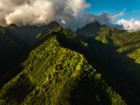 Aerial view of lush green mountain ridges and dramatic peaks under a cloudy sky during golden hour Moorea Maiao Windward Islands French Polynesia. Aerial view of lush green mountain ridges and dramatic peaks under a cloudy sky during golden hour Moorea Maiao Windward Islands French Polynesia.
