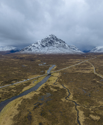 Aerial view of River Etive Bridge and the snow capped Buachaille Etive Mor mountain with a winding river through the brown moorland Ballachulish Scotland United Kingdom. Aerial view of River Etive Bridge and the snow capped Buachaille Etive Mor mountain with a winding river through the brown moorland Ballachulish Scotland United Kingdom.