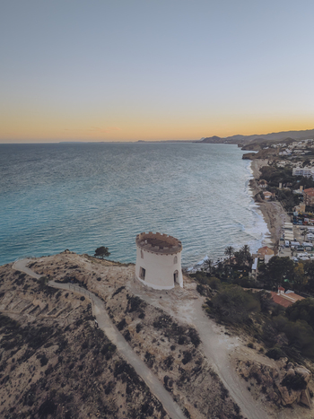 Aerial view of Santuari iber i roma de la Malladeta on a rocky cliff overlooking the Mediterranean coastline and sandy beaches at sunset La Vila Joiosa Comunidad Valenciana Spain. Aerial view of Santuari iber i roma de la Malladeta on a rocky cliff overlooking the Mediterranean coastline and sandy beaches at sunset La Vila Joiosa Comunidad Valenciana Spain.