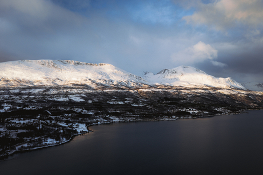 Aerial view of snow capped mountains meeting the dark waters edge under a moody sky Sjøvegan Troms Norway. Aerial view of snow capped mountains meeting the dark waters edge under a moody sky Sjøvegan Troms Norway.
