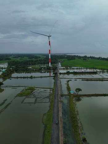 Aerial view of the Khurushkul wind turbine rising above flooded agricultural fields and fish farms along a straight road in Cox s Bazar Chittagong Division Bangladesh. Aerial view of the Khurushkul wind turbine rising above flooded agricultural fields and fish farms along a straight road in Cox s Bazar Chittagong Division Bangladesh.