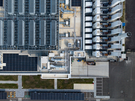 Aerial view of a modern data center campus featuring industrial cooling units solar panel arrays and paved parking areas in Melegnano Lombardy Italy.