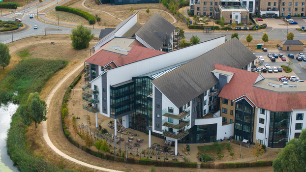 Aerial view of Wixams Retirement Village featuring modern architecture with pitched roofs and glass facades surrounded by landscaped grounds and a pond in Bedford England United Kingdom.